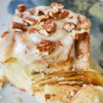 Sticky, sweat cinnamon roll with pecans being eaten with a fork