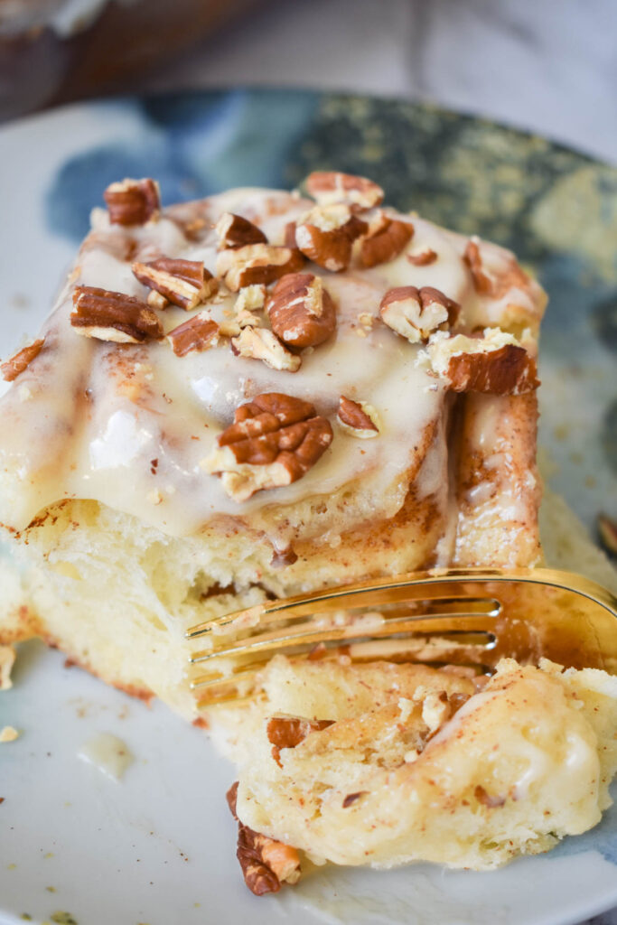 Sticky, sweat cinnamon roll with pecans being eaten with a fork