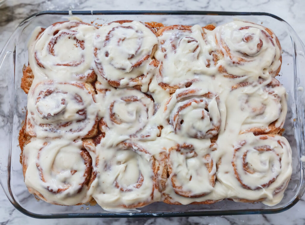 Baked cinnamon rolls with cream cheese frosting on top in pan